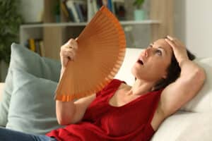 Adult woman fanning suffering heat stroke sitting in the livingroom at home